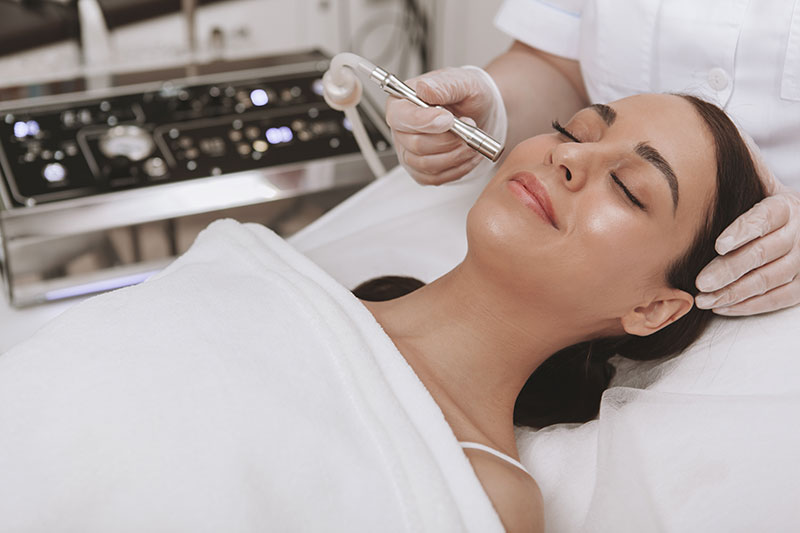 Professional cosmetologit performing microdermabrasion procedure on the face